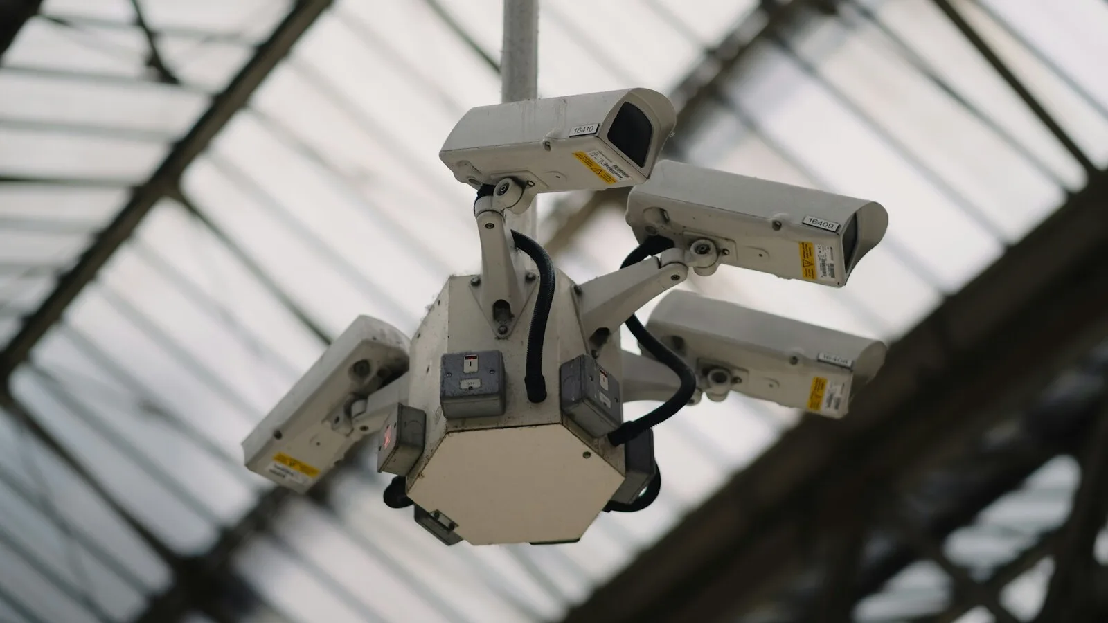 A cluster of CCTV cameras mounted beneath a glass roof, angled to cover the space below.