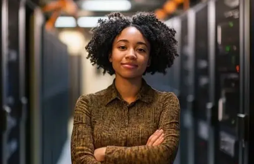 Woman working inside a server room surrounded by network equipment.