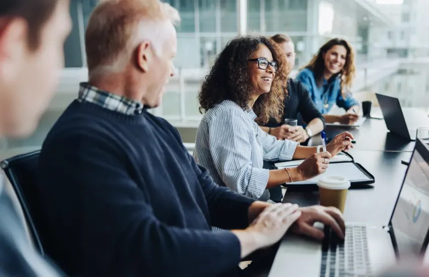 Diverse team of cleared professionals collaborating around a conference table with laptops during a security briefing meet...