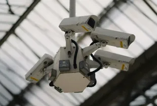 A cluster of CCTV cameras mounted beneath a glass roof, angled to cover the space below.